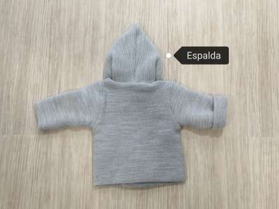 La espalda de la chaqueta es lisa en color gris y viene con gorro