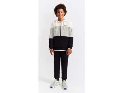 Un niño nos enseña el conjunto de dos piezas con chaqueta abierta y pantalón negro a juego